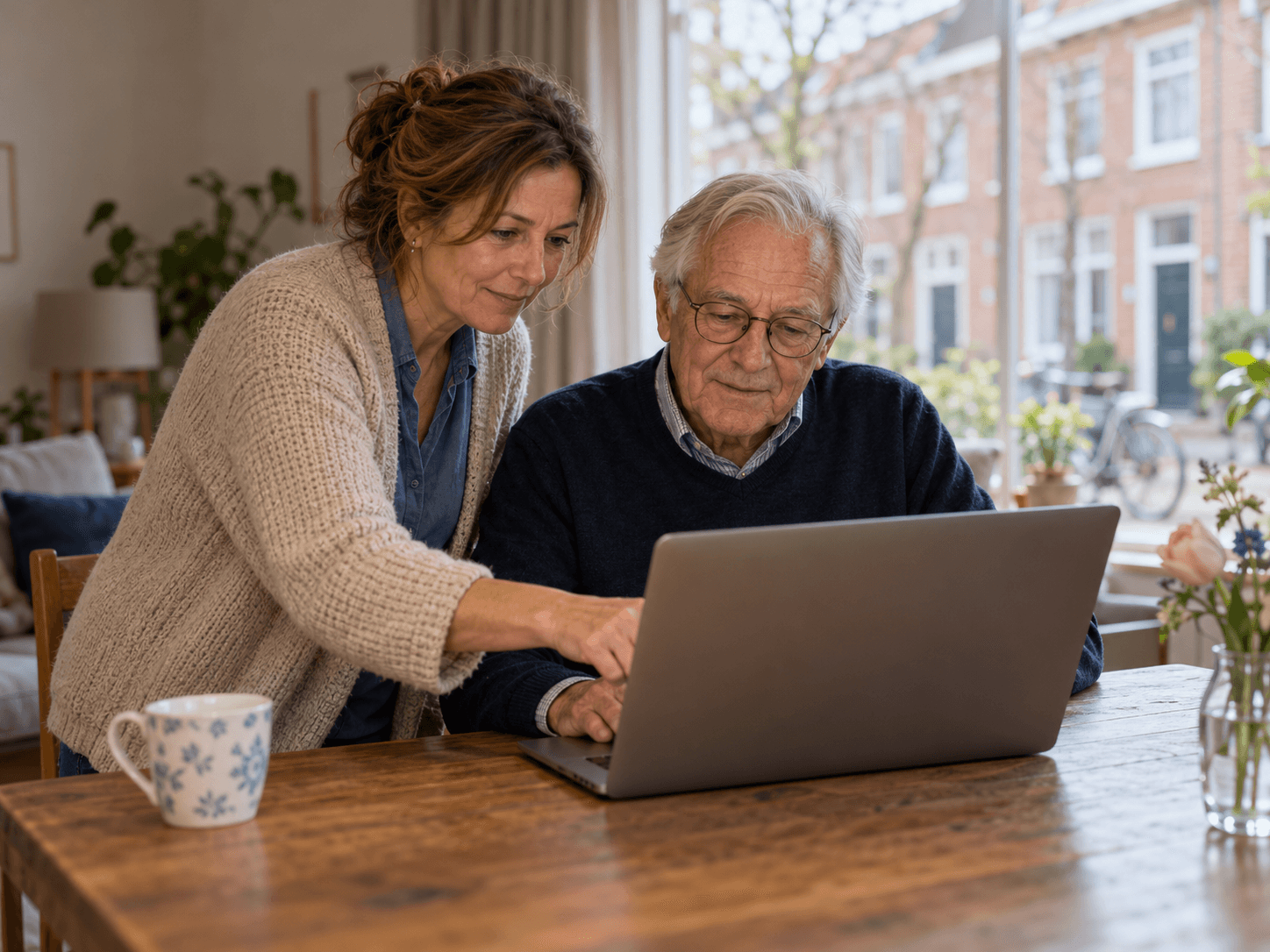 Een vrouw helpt een oudere man bij het gebruik van een laptop.